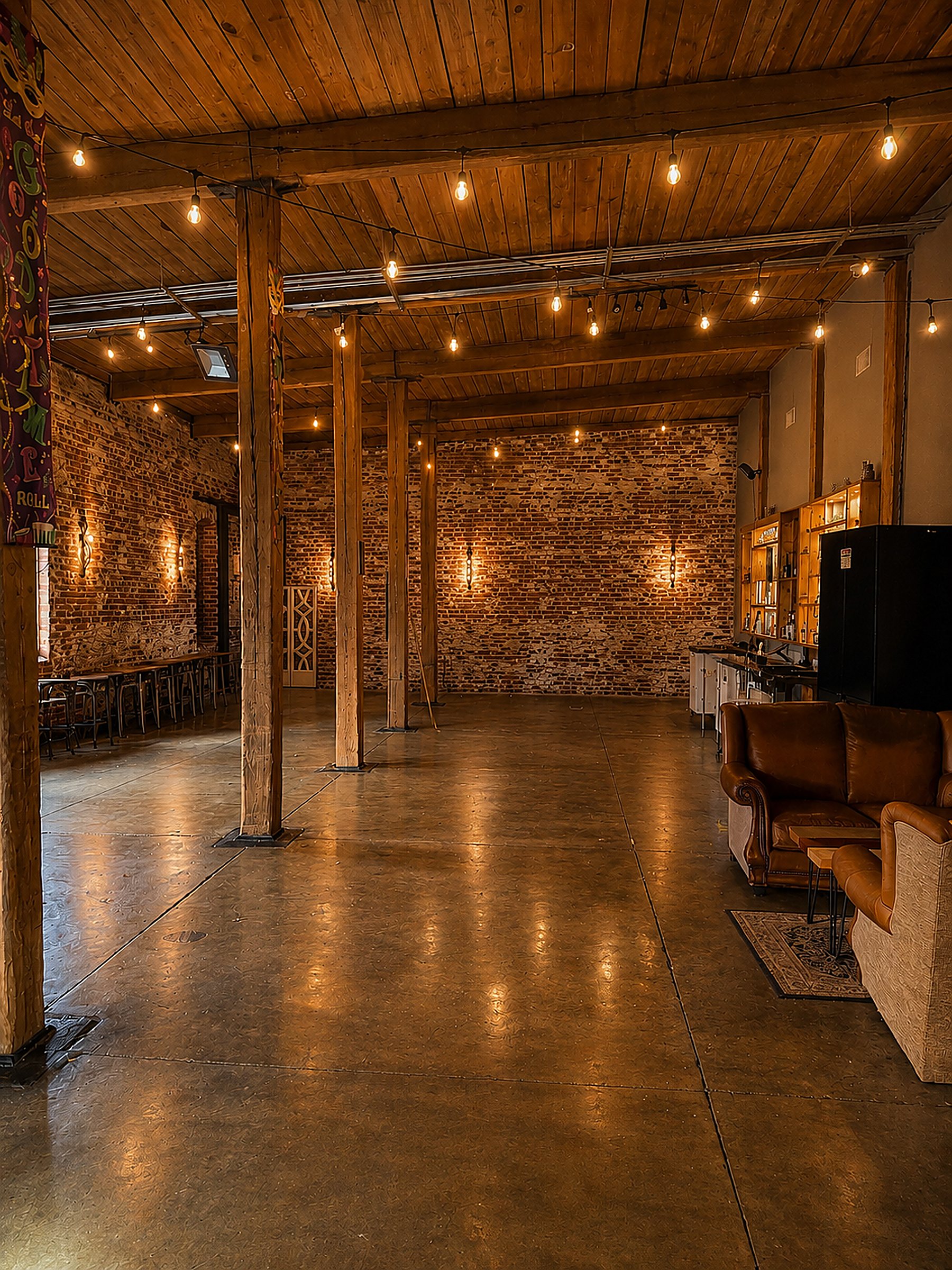 Suite G open event hall — café string lights under wood-plank ceilings, exposed brick and leather lounge seating