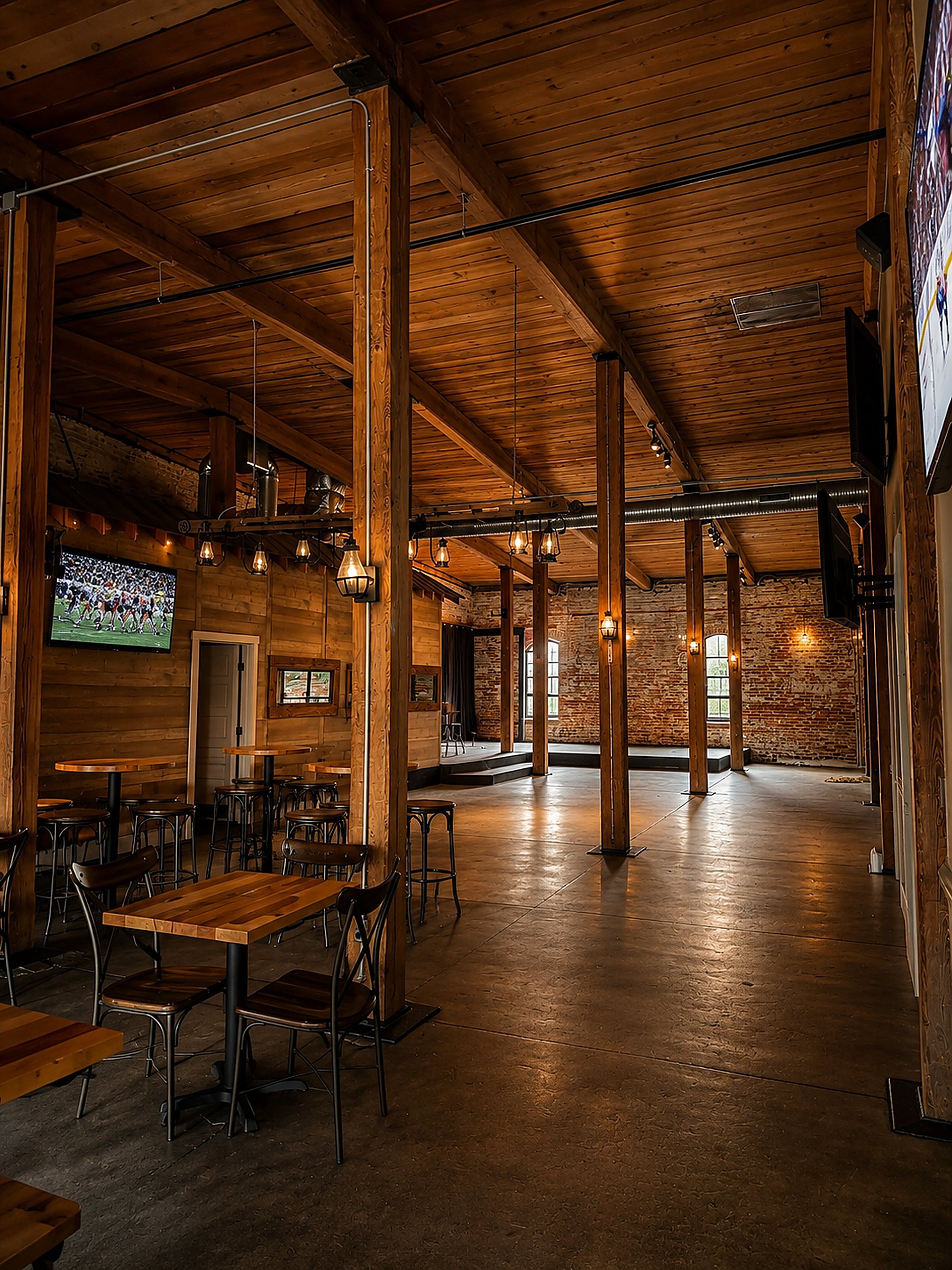 Suite G stage and sports lounge — mounted TVs, raised stage wired for live music, reclaimed wood and communal high-tops